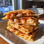 A stack of four golden-brown, crispy shrimp quesadilla wedges overflowing with cheesy shrimp filling.