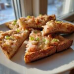Close-up of golden brown shrimp toast triangles topped with minced shrimp and sliced green onions, served on a light plate.