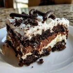 A close-up slice of layered dirt cake featuring chocolate pudding, whipped cream, and crumbled cookies.