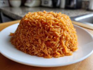 A mound of vibrant, orange-red smoky jollof rice served neatly on a white plate.