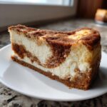 A perfect slice of snickerdoodle cheesecake showing a creamy white filling swirled with cinnamon streusel topping and crust.