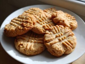 A plate of freshly baked, soft peanut butter cookies featuring the classic crisscross fork marks.