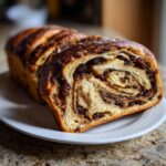 A close-up of a freshly baked loaf of soft raisin bread, showing a beautiful swirl pattern filled with raisins.
