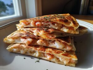 Four stacked, golden-brown wedges of shrimp quesadilla filled with pink shrimp and melted cheese, garnished with herbs.