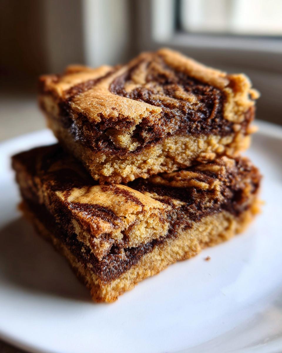 Close-up of two stacked snickerdoodle blondies featuring a rich, marbled cinnamon swirl pattern on a white plate.