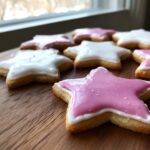 Close-up of star-shaped sugar cookies decorated with pink and white sugar cookie icing recipe, resting on a wooden surface.