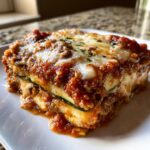A close-up of a hearty slice of zucchini lasagna layered with meat sauce, ricotta, and melted mozzarella cheese.