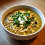 Close-up of a bowl of creamy chicken enchilada soup with shredded chicken, corn, black beans, and cilantro.