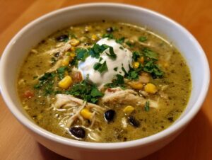 A close-up of a bowl of creamy chicken enchilada soup topped with sour cream, cilantro, corn, and black beans.