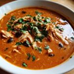 Close-up of a bowl of creamy chicken enchilada soup healthy, topped with shredded chicken, black beans, and cilantro.