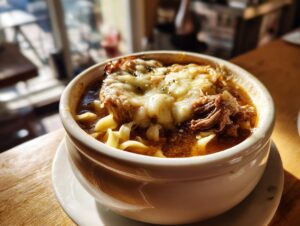 A bowl of rich crockpot french onion soup beef and noodles topped with melted cheese and crouton.