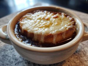 Close-up of a bowl of crockpot french onion soup topped with a thick slice of toasted bread and melted, bubbly Gruyère cheese.