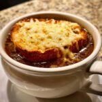 Close-up of rich crockpot french onion soup topped with a thick, cheesy, broiled crouton.