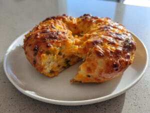 A golden-brown jalapeno cheddar sourdough discard bagel with a piece broken off, showing cheesy interior.
