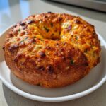 A freshly baked jalapeno cheddar sourdough discard bagel with a golden, cheesy crust, resting on a white plate.