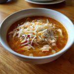 A white bowl filled with keto creamy chicken enchilada soup, topped generously with shredded cheese.