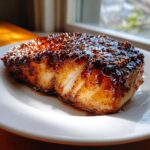 A thick fillet of miso glazed chilean sea bass recipe, caramelized and glossy on a white plate.