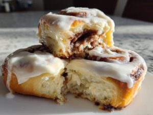 Close-up of three gooey overnight sourdough discard cinnamon rolls stacked, drizzled with thick white icing.