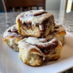 A stack of four gooey overnight sourdough discard cinnamon rolls topped with thick white icing.