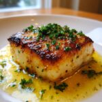 Close-up of a perfectly pan seared chilean sea bass recipe fillet topped with fresh parsley and sitting in a lemon butter sauce.