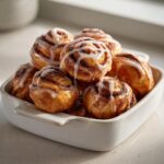 A white dish overflowing with freshly baked sourdough discard cinnamon roll bites drizzled with white icing.