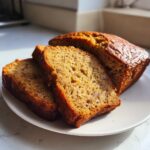Close-up of three thick slices of moist flourless peanut butter banana bread next to the remaining loaf on a white plate.