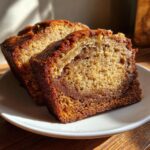 Two moist slices of gluten free peanut butter banana bread served on a white plate, showing a rich brown crust.