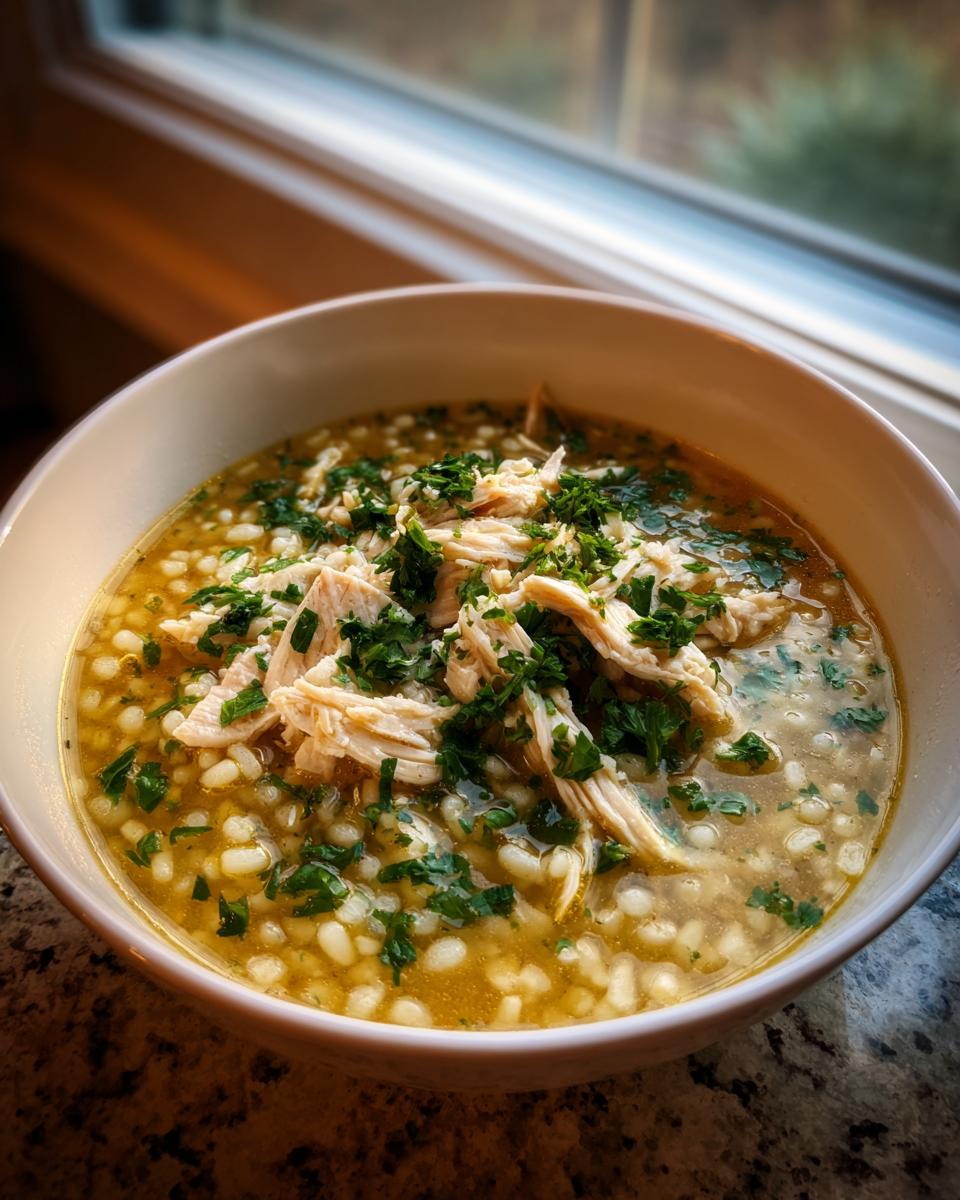 A close-up of a bowl of comforting italien penicillin soup, featuring small pasta shapes, shredded chicken, and fresh parsley.